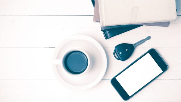 coffee cup with phone,car key and stack of book on white wood table vintage style
