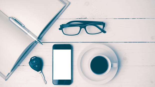coffee cup with phone, car key,eyeglasses and open notebook on white wood table vintage style
