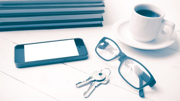 coffee cup with phone,key,eyeglasses and stack of book on white wood table vintage style