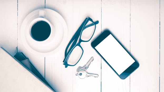 coffee cup with phone,key,eyeglasses and stack of book on white wood table vintage style