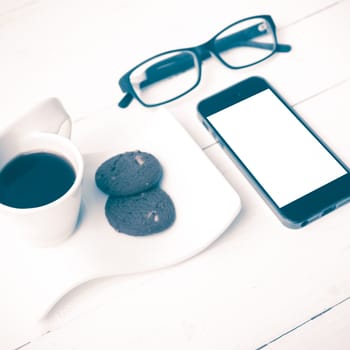 coffee cup with cookie,phone and eyeglasses on white wood table vintage style