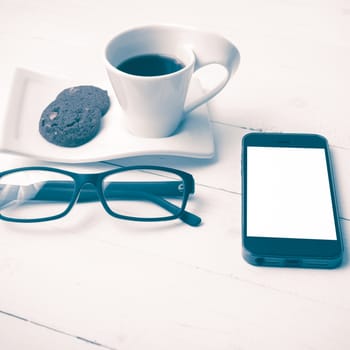 coffee cup with cookie,phone and eyeglasses on white wood table vintage style