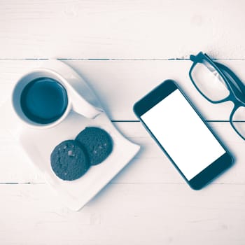 coffee cup with cookie,phone and eyeglasses on white wood table vintage style