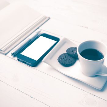coffee cup with cookie,phone with notebook and pen on white wood table vintage style