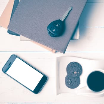 coffe cup with cookie,phone,car key and stack of book on white wood table vintage style