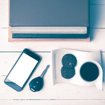 coffe cup with cookie,phone,car key and stack of book on white wood table vintage style