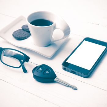 coffee cup with cookie,phone,eyeglasses and car key on white wood table vintage style