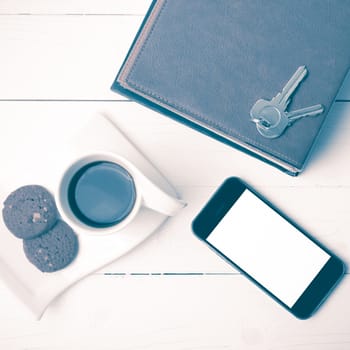 coffee cup with cookie,phone,stack of book and key on white wood table vintage style