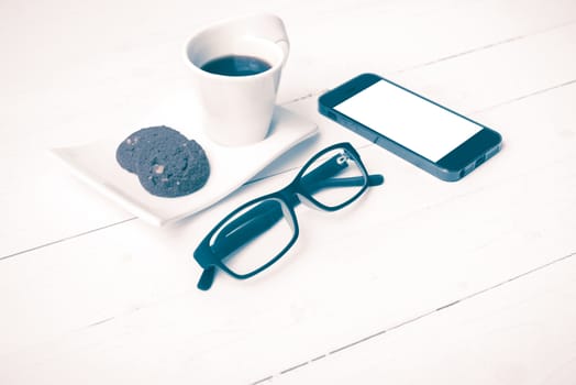 coffee cup with cookie,phone and eyeglasses on white wood table vintage style