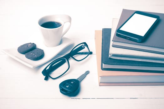 coffe cup with cookie,phone,car key,eyeglasses and stack of book on white wood table vintage style