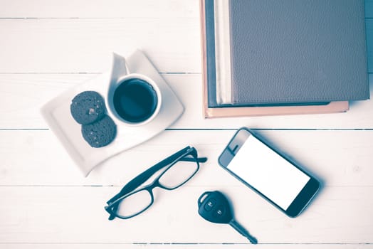 coffe cup with cookie,phone,car key,eyeglasses and stack of book on white wood table vintage style