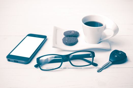 coffee cup with cookie,phone,eyeglasses and car key on white wood table vintage style