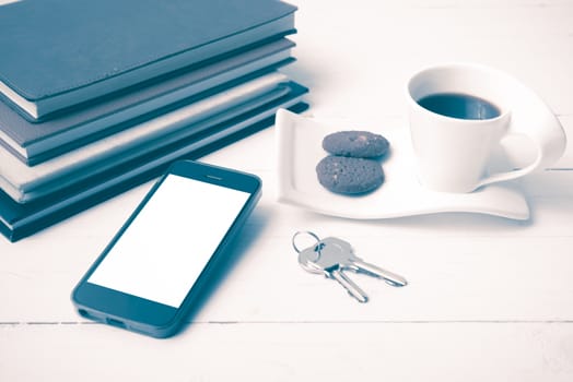 coffee cup with cookie,phone,stack of book and key on white wood table vintage style