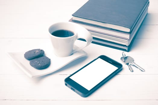 coffee cup with cookie,phone,stack of book and key on white wood table vintage style