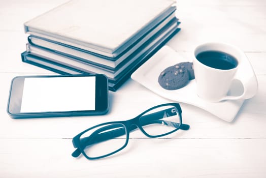 coffee cup with cookie,phone,stack of book and eyeglasses on white wood table vintage style