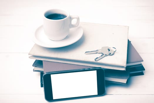 coffee cup with phone,key and stack of book on white wood table vintage style