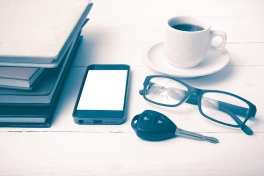 coffee cup with phone, car key,eyeglasses and stack of book on white wood table vintage style