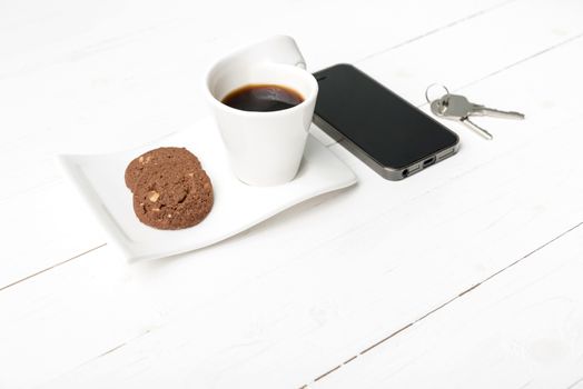 coffee cup with cookie,phone and key on white wood table