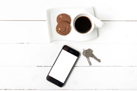 coffee cup with cookie,phone and key on white wood table