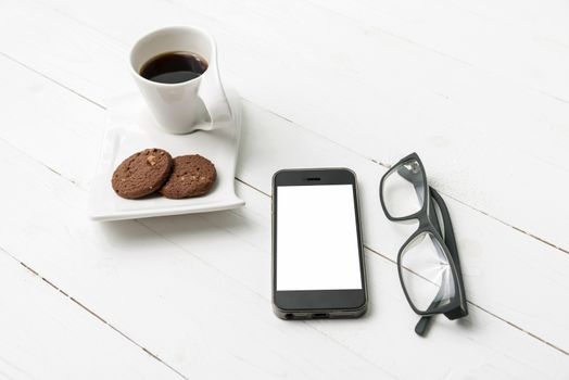 coffee cup with cookie,phone and eyeglasses on white wood table