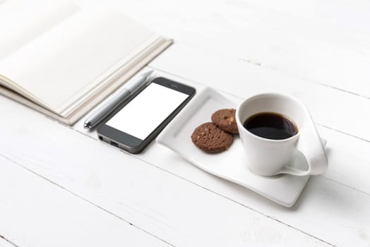 coffee cup with cookie,phone with notebook and pen on white wood table