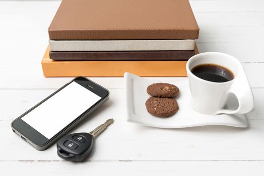 coffe cup with cookie,phone,car key and stack of book on white wood table
