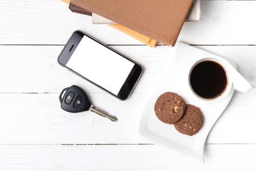 coffe cup with cookie,phone,car key and stack of book on white wood table