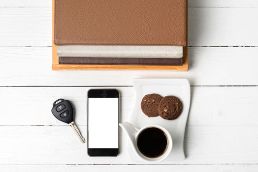 coffe cup with cookie,phone,car key and stack of book on white wood table