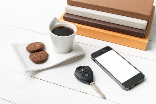 coffe cup with cookie,phone,car key and stack of book on white wood table