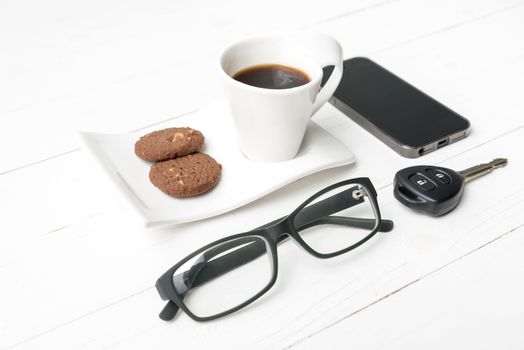 coffee cup with cookie,phone,eyeglasses and car key on white wood table