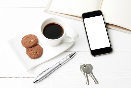 coffee cup with cookie,phone,notebook and key on white wood table