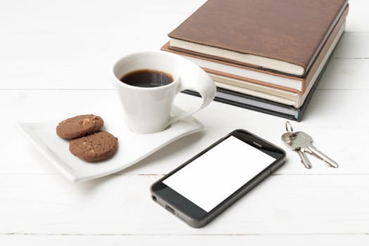 coffee cup with cookie,phone,stack of book and key on white wood table