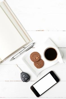 coffee cup with cookie,phone,open notebook and car key on white wood table