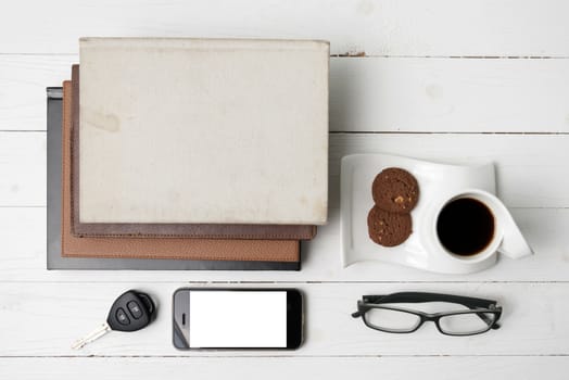 coffee cup with cookie,phone,stack of book and car key on white wood table