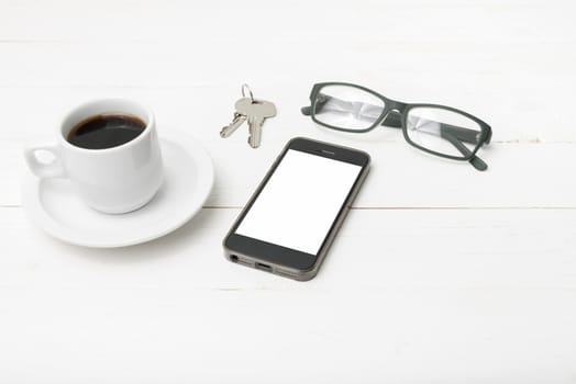 coffee cup with phone, eyeglasses and key on white wood table