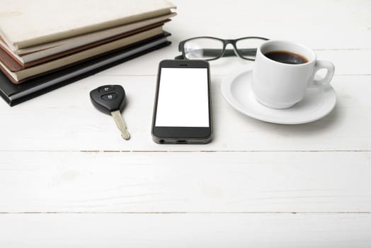 coffee cup with phone, car key,eyeglasses and stack of book on white wood table
