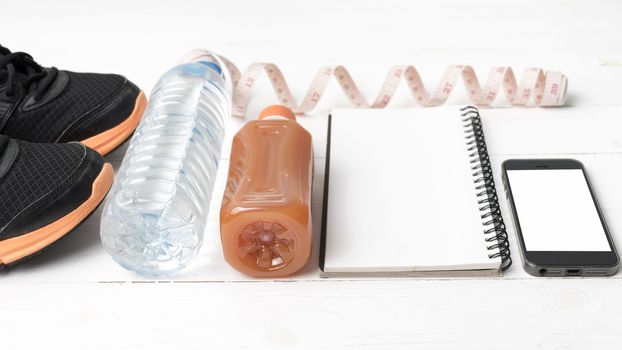 fitness equipment:running shoes,water,measuring tape,notepad,phone and juice on white wood background