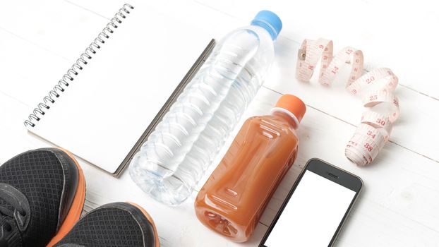 fitness equipment:running shoes,water,measuring tape,notepad,phone and juice on white wood background