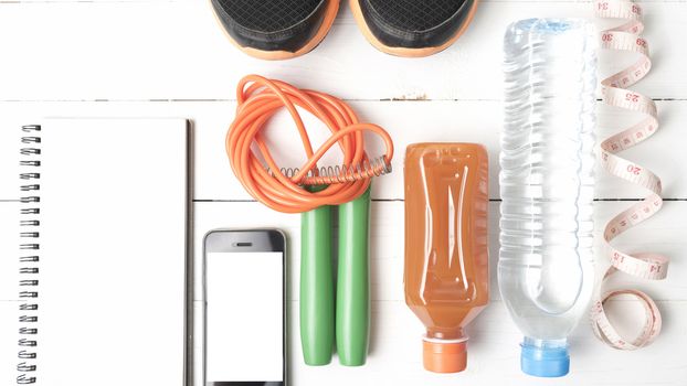 fitness equipment:running shoes,jumping rope,notepad,phone,water,juice and measuring tape on white wood background