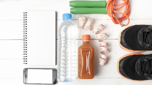 fitness equipment:running shoes,jumping rope,notepad,phone,water,juice and measuring tape on white wood background