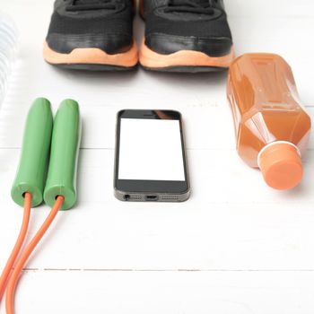 fitness equipment : running shoes,jumping rope,water,juice and phone on white wood background