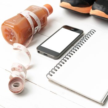 fitness equipment:running shoes,juice,measuring tape,notepad and phone on white wood background