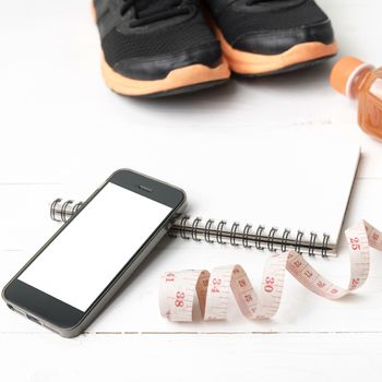 fitness equipment:running shoes,juice,measuring tape,notepad and phone on white wood background