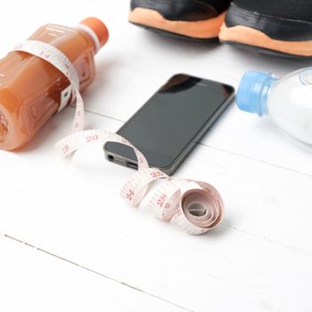 fitness equipment:running shoes,measuring tape,water,juice and phone on white wood background