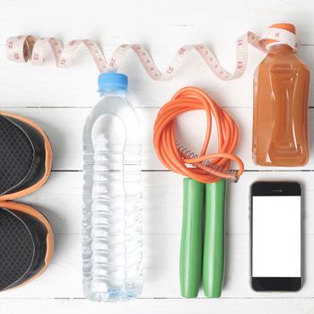 fitness equipment:running shoes,phone,measuring tape,water,juice and jumpong rope on white wood background