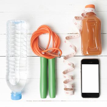 fitness equipment:running shoes,phone,measuring tape,water,juice and jumpong rope on white wood background