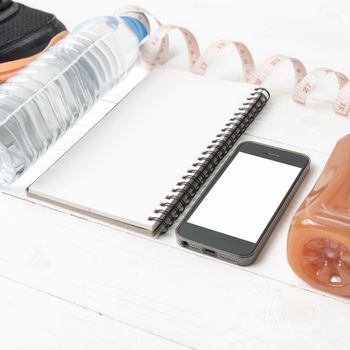 fitness equipment:running shoes,water,measuring tape,notepad,phone and juice on white wood background