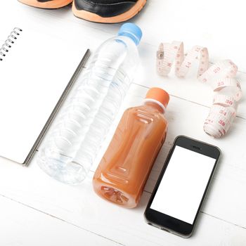 fitness equipment:running shoes,water,measuring tape,notepad,phone and juice on white wood background