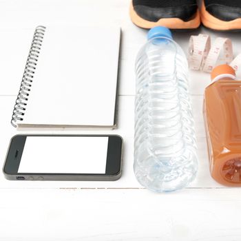 fitness equipment:running shoes,water,measuring tape,notepad,phone and juice on white wood background