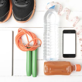 fitness equipment:running shoes,jumping rope,notepad,phone,water,juice and measuring tape on white wood background